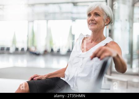 Lächelnde Seniorin, die im Wartebereich sitzt und sich umsieht Stockfoto