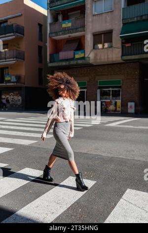 Junge Frau mit Afro Frisur Überqueren der Straße in der Stadt Stockfoto