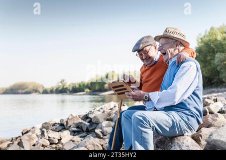 Zwei alte Freunde sitzen am Flussufer, mit digitalen Tablet Stockfoto