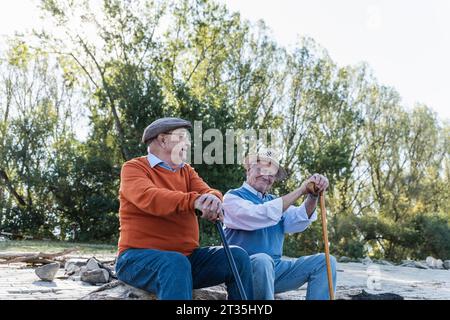 Zwei alte Freunde sitzen auf einem Baumstamm am Flussufer, Teilen von Erinnerungen Stockfoto