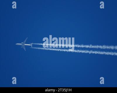 Tele Nahaufnahme eines Flugzeugs, das in großer Höhe mit Kondensstreifen in einem klaren blauen Himmel fliegt Stockfoto