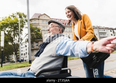 Lachende junge Frau drückt gerne älterer Mann im Rollstuhl Stockfoto