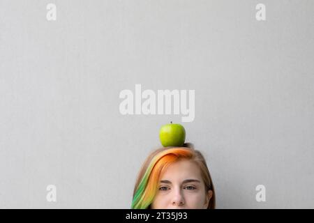 Teenager-Mädchen, das Apfel auf dem Kopf vor grauem Hintergrund balanciert Stockfoto