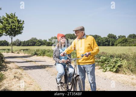 Glücklicher Großvater mit Enkelin, die auf dem Feld auf dem Fahrrad sitzt Stockfoto