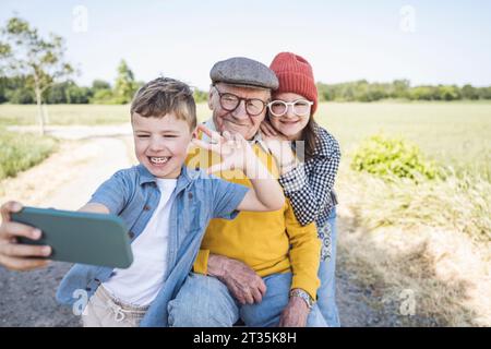 Glücklicher Junge, der Selfie mit Schwester und Großvater über das Smartphone macht Stockfoto