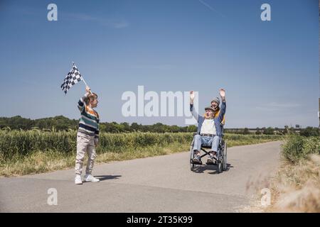 Junge mit karierter Flagge und Senior-Mann im Rollstuhl auf der Straße Stockfoto