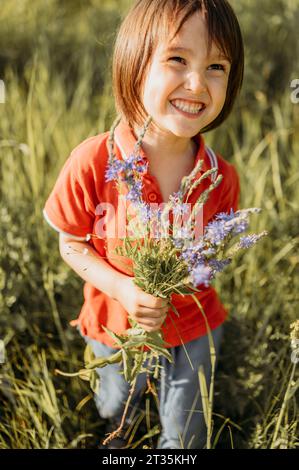 Ein lächelnder Junge, der Blumen auf dem Feld hält Stockfoto