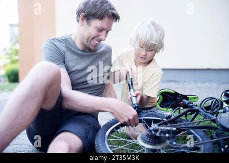 Glücklicher Vater und Sohn mit Pumpe, die Fahrrad am Fußweg reparieren Stockfoto
