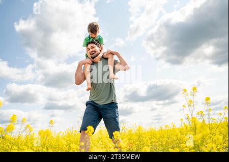 Fröhlicher Vater, der Sohn trägt und im Feld läuft Stockfoto
