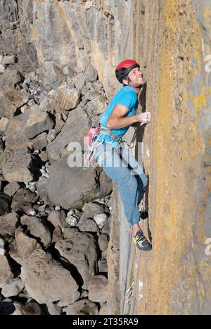 Entschlossener Mann, der einen felsigen Berg an sonnigem Tag klettert Stockfoto