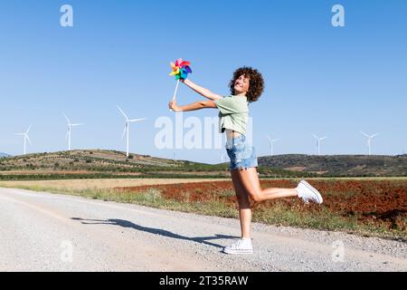 Glückliche Frau, die mit mehrfarbigem Windradspielzeug vor Windrädern steht Stockfoto