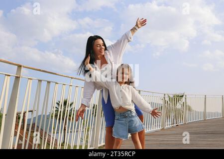 Glückliche Mutter und Tochter tanzen mit erhobenen Armen an sonnigen Tagen Stockfoto