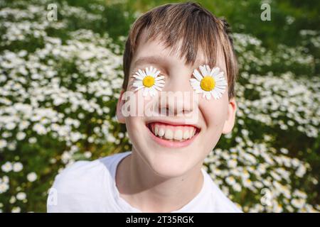 Glücklicher Junge mit Kamillenblüten über den Augen Stockfoto