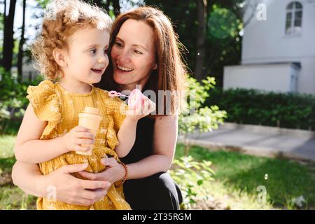 Lächelnde Mutter, die die Tochter ansieht, die einen Bubble-Zauberstab hält Stockfoto