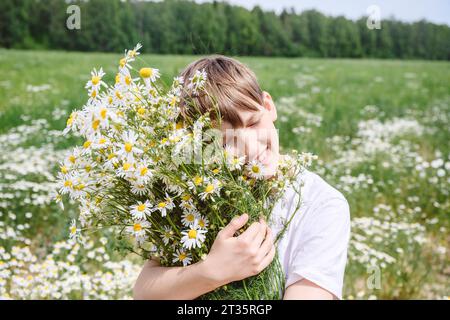 Lächelnder Junge mit geschlossenen Augen, der Kamillenblüten hält Stockfoto