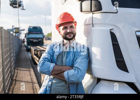 Kontemplativer Lkw-Fahrer mit überkreuzten Armen, der auf den Lkw gelehnt ist Stockfoto