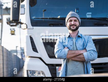 Selbstbewusster Lkw-Fahrer mit überkreuzten Armen vor dem Lkw stehend Stockfoto