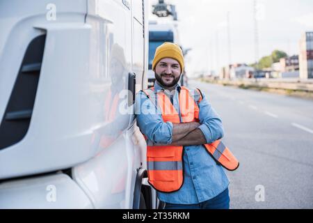 Lächelnder Lkw-Fahrer mit überkreuzten Armen, lehnend auf den Lkw Stockfoto