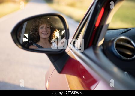 Reflexion der glücklichen Frau im Seitenspiegel des Autos Stockfoto