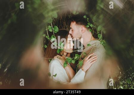 Ein romantischer Freund küsst die Stirn der Freundin in der Nähe von Pflanzen Stockfoto