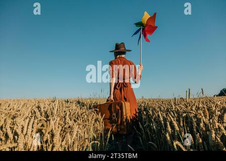 Frau in braunem Kleid, die auf dem Weizenfeld ein Windradspielzeug hält Stockfoto