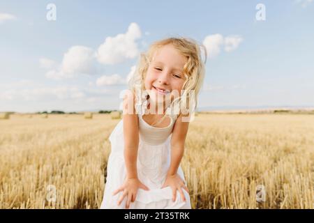 Glückliches blondes Mädchen, das auf einem Stoppelfeld steht und Hände auf den Knien hat Stockfoto