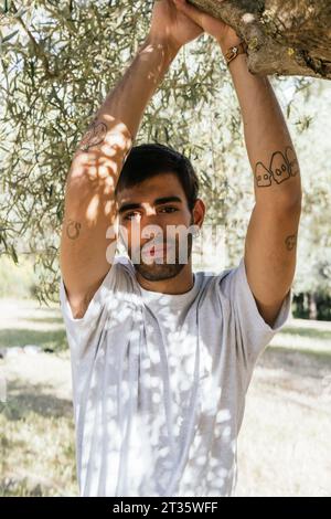 Junger Mann, der am sonnigen Tag unter einem Baum steht Stockfoto