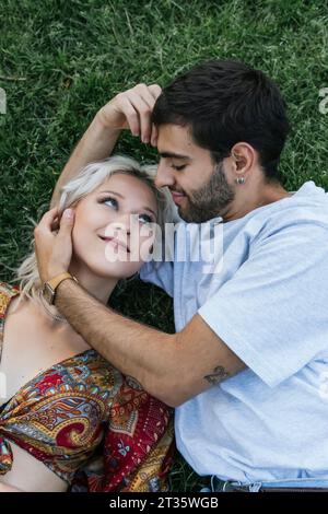 Liebevolles junges Paar, das im Park auf Gras liegt Stockfoto