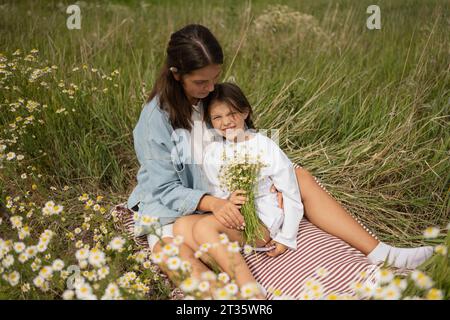 Mutter und Tochter sitzen mit einem Haufen Gänseblümchen an sonnigen Tagen Stockfoto