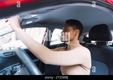 Glückliche junge Frau, die den Rückspiegel im Auto verstellt Stockfoto