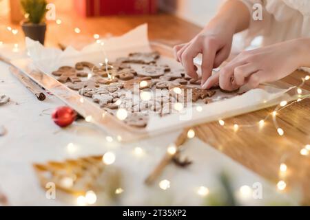 Frau, die Lebkuchenkekse in der Nähe von Lichtern auf dem Tisch zu Hause macht Stockfoto