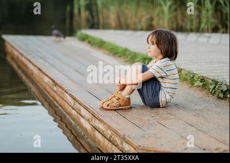 Besinnlicher Junge, der in der Nähe des Sees sitzt Stockfoto