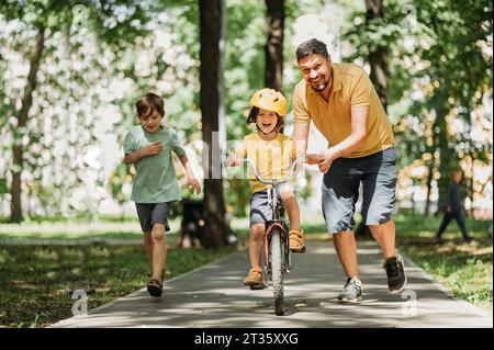 Glücklicher Vater, der seinem Sohn hilft, im Park Fahrrad zu fahren Stockfoto