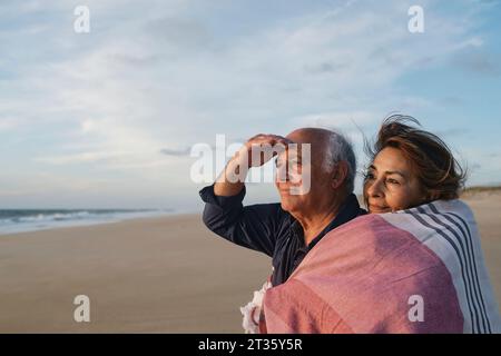 Lächelnder Seniorenmann und Frau in Schal am Strand Stockfoto