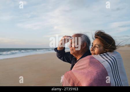 Lächelnde Seniorin umarmt Mann am Strand Stockfoto