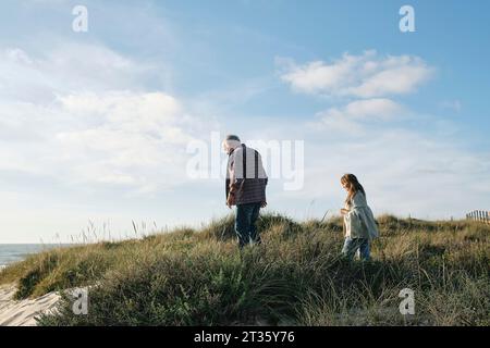 Senior Mann und Frau, die an sonnigen Tagen zwischen Pflanzen am Strand spazieren gehen Stockfoto