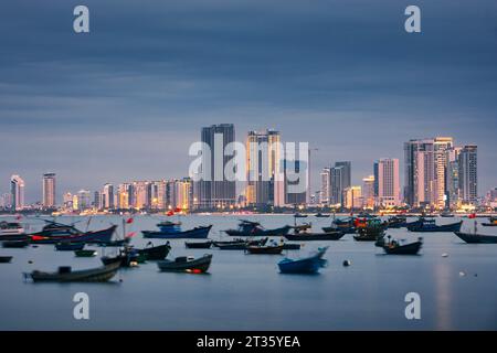 Da Nang Stadtbild in der Dämmerung. Das Fischerboot liegt im Hafen vor der beleuchteten Küste mit modernen Gebäuden. Stockfoto