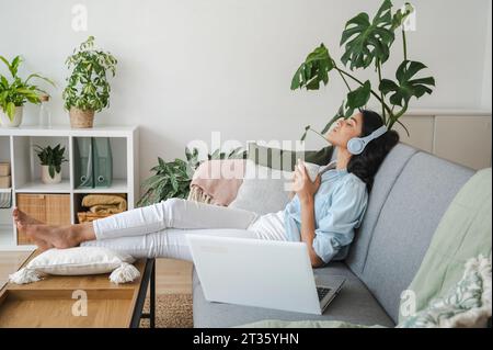 Junge Frauen, die zu Hause eine Kaffeetasse halten und sich auf dem Sofa entspannen Stockfoto
