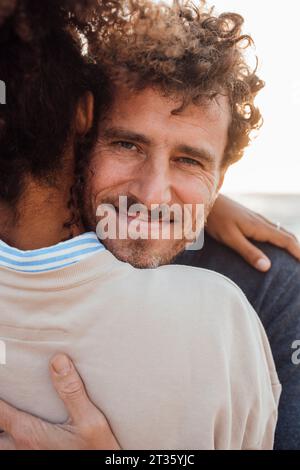 Lächelnder Mann, der seine Freundin am Strand umarmt Stockfoto