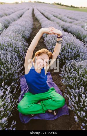 Lächelnde Frau, die Yoga-Übungen im Lavendelfeld macht Stockfoto