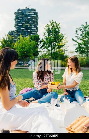 Glückliche Frau mit Freunden, die an sonnigem Tag eine Geschenkbox halten Stockfoto