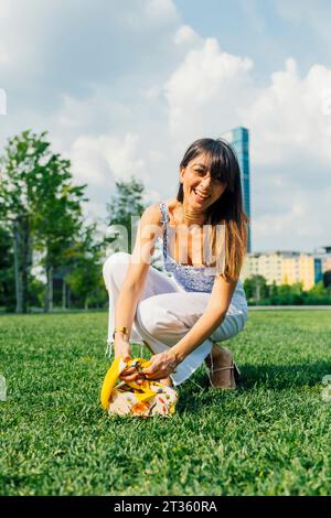 Glückliche Frau, die sich unter bewölktem Himmel auf Gras hockt Stockfoto