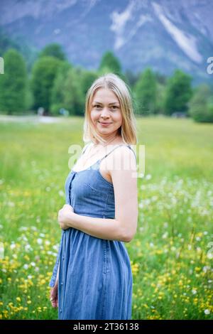 Lächelnde Frau in blauem Kleid, die auf der Wiese steht Stockfoto