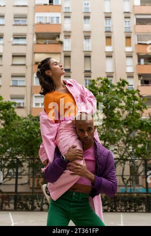 Nicht-binäre Person, die Frau auf Schultern vor dem Gebäude trägt Stockfoto