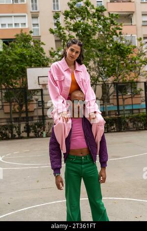 Frau, die auf den Schultern einer nicht-binären Person auf dem Basketballfeld sitzt Stockfoto