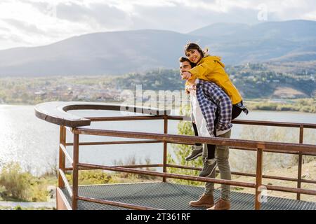 Der Freund reitet mit Huckepack zu seiner Freundin, die auf dem Beobachtungspunkt steht Stockfoto