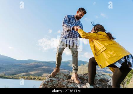 Freund hilft Freundin beim Klettern auf Felsen Stockfoto