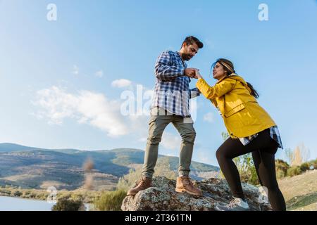 Der Freund hält die Hände einer Freundin, die auf den Felsen klettert Stockfoto