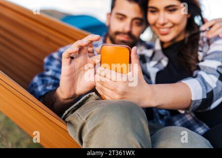 Mann und Frau surfen im Netz durch Smartphone, sitzen in der Hängematte Stockfoto