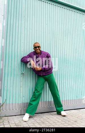 Glückliche, nicht-binäre Person mit Sonnenbrille, die vor der blauen Tür steht Stockfoto